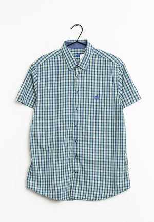 Chemise à manches courtes boutonnée avec motif à carreaux bleu, vert et blanc suspendue sur un cintre noir sur fond blanc.