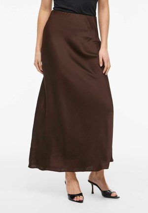 Femme portant une jupe en satin marron foncé longueur cheville, associée à des sandales à talons hauts ouvertes noires et un haut noir.