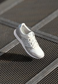 Grey and white athletic shoe with mesh and suede materials, featuring a textured upper, rounded toe, and lace-up design.
