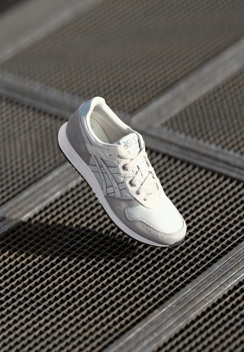 Grey and white athletic shoe with mesh and suede materials, featuring a textured upper, rounded toe, and lace-up design.