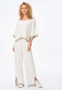 V-hals, kort mouwtop en wijde broek in off-white met contrasterende beige afwerking. Zachte stof met een ontspannen pasvorm en zijsplitten op de broek.