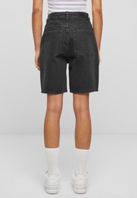 Pantalones cortos de mezclilla negra con cintura alta, bolsillos traseros planos y bordes sin terminar, combinados con zapatillas blancas y calcetines de longitud media.