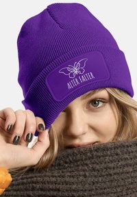 Purple knitted beanie with a textured pattern and a rectangular patch featuring a butterfly design and "ALTER FALTER" text.