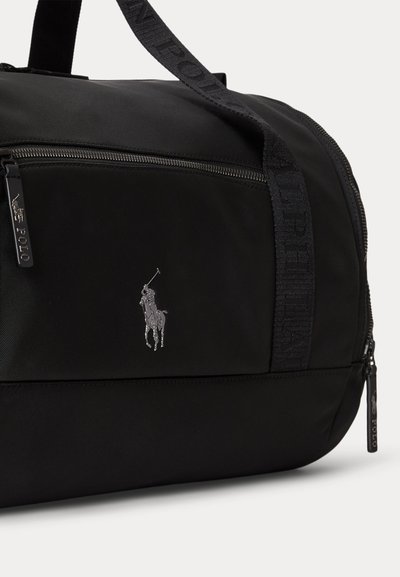 Черна спортна чанта с преден цип джоб, лого Polo Ralph Lauren и брандирани дръжки от плат, видими на обикновен фон.