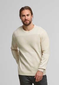 Maglione crema a trama con una parte superiore liscia e una metà inferiore a fantasia, caratterizzato da un collo rotondo e polsini e orlo a coste.