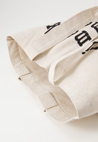 Leinen-Tote-Bag in hellbeige mit schwarzem Text. Verfügt über robuste Griffe und eine strukturierte Form mit einer glatten Textur.