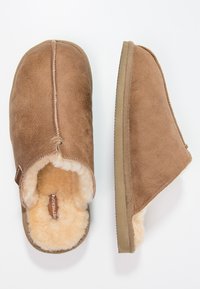 Brown suede slippers with a soft, beige shearling lining and rubber outsole. Features a stitched seam along the upper. Open-back design.