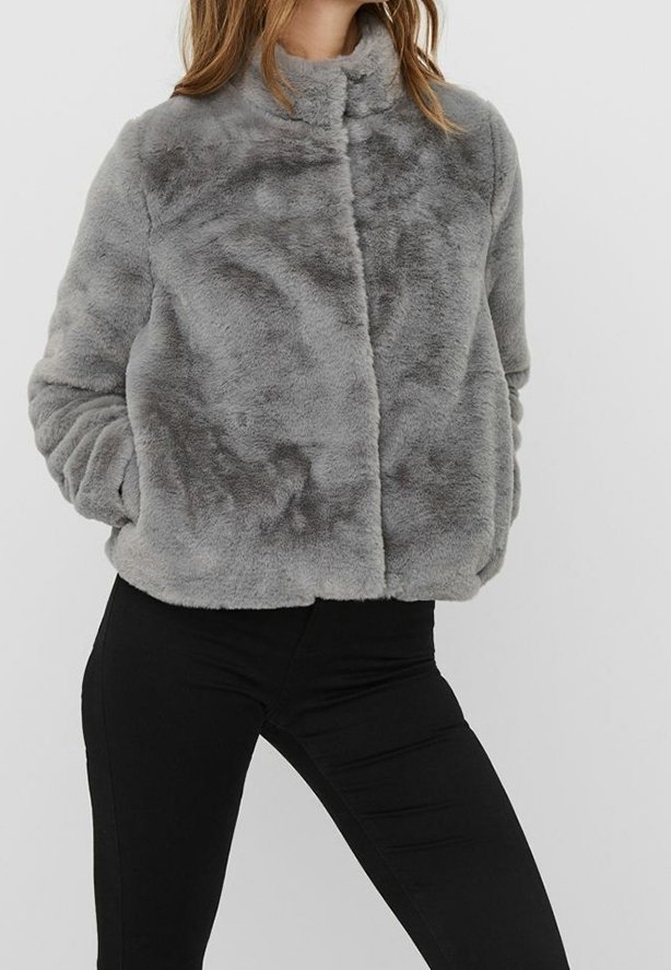 Szara sztuczna futrzana kurtka z wysokim kołnierzem, zapięcie z przodu oraz miękka tekstura. Nosiwana na czarnych dopasowanych spodniach.