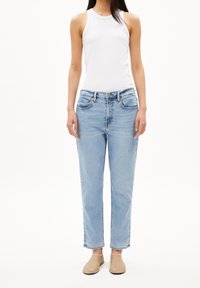 Vaaleansiniset suorat korkeavyötäröiset farkut, joissa etutaskut ja kulutettu pinta, yhdistetty valkoiseen hihattomaan toppiin.