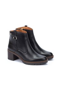 Bottes chelsea en cuir noir avec une finition lisse, bout rond et talon large. Elles présentent une fermeture éclair sur le côté et une sangle décorative avec un accent métallique.