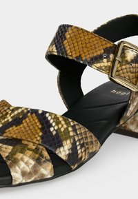 Ανοιχτό πέδιλο με λουράκια από καφέ και μαύρη φιδίσια επιδερμίδα, χρυσή αγκράφα και μαύρο μαλακό πάτο με ραφές.