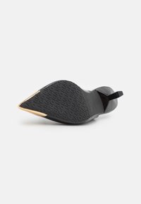 Chaussure à talon haut noire avec un bout pointu, un matériau supérieur lisse et une semelle noire texturée avec des détails de logo ; accent métallique sur le bout.