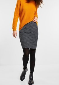 Pomarańczowy sweter o fakturze, szara spódnica o wzorze zygzaka, czarne rajstopy i czarne botki za kostkę. Skupienie na kształtach ubrań i wzorach.