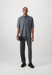 Short-sleeve checkered shirt in navy and white, with a pocket, paired with gray trousers and black sneakers.