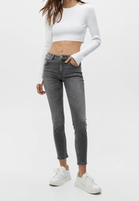 Haut court blanc côtelé associé à un jean skinny gris taille haute. Le modèle porte des baskets blanches ; conception simple, coupe ajustée, avec un minimum de détails.