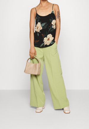 Débardeur noir à motif floral avec fines bretelles spaghetti, associé à un pantalon large vert clair. Accessoire : petit sac tressé beige. Chaussures beiges.