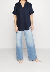 Granatowa lniana bluzka z krótkim rękawem i dekoltem w serek, w połączeniu z jasnoniebieskimi spodniami typu wide-leg i beżowymi szpilkami w szpic. Prosty design i luźny krój.