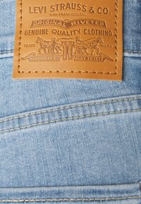 Parche de cuero marrón claro en denim azul claro que presenta texto y gráficos en relieve, incluidos caballos y el nombre de la marca "Levi Strauss & Co."