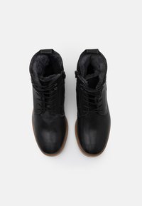 Botas de tobillo de cuero negro con un acabado suave, forro texturizado, cordones en la parte delantera y suela de goma marrón claro. Incluye ojales de metal.