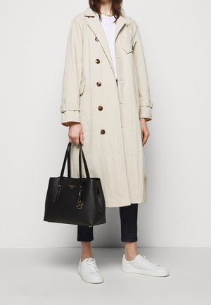 Beige trenchcoat med brune knapper, sort læder tote bag med gyldne detaljer, mørke jeans og hvide sneakers. Enkelt og funktionelt design.
