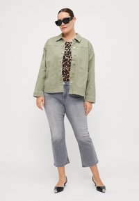 Light green denim jacket with two front pockets, worn over a leopard print top, paired with gray flared jeans and black pointed-toe shoes.