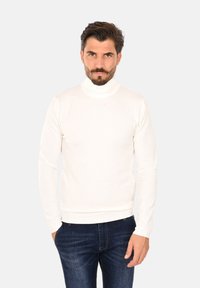 Maglione bianco a collo alto realizzato in un materiale liscio, dalla forma aderente e con polsini a coste. Abbinato a jeans in denim scuro con una leggera consistenza.