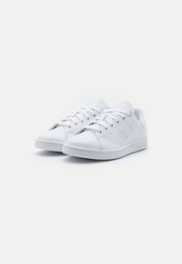 Baskets blanches en cuir avec une texture lisse, présentant des accents perforés, un système de laçage et une semelle en caoutchouc plate.
