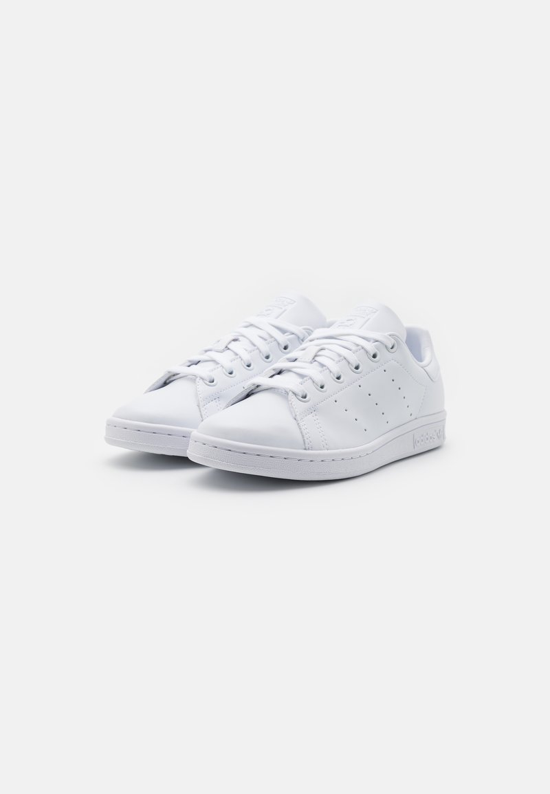 Baskets blanches en cuir avec une texture lisse, présentant des accents perforés, un système de laçage et une semelle en caoutchouc plate.