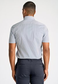Camicetta a maniche corte di colore blu chiaro con un piccolo motivo geometrico, abbinata a pantaloni scuri di colore blu navy con tasche posteriori e hardware minimale.