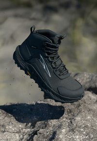 Svart vanntett turstøvler med mesh-overdel, teksturert overflate, høy ankelstøtte og Vibram-såle for godt grep på steinete terreng.