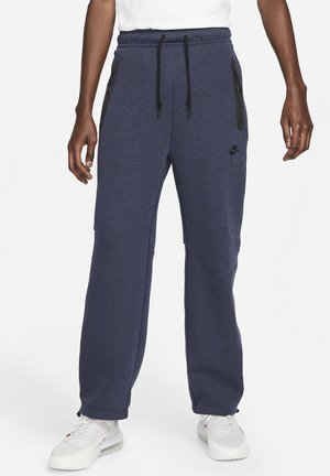 Pantaloni sportivi Nike blu navy con vita elasticizzata e coulisse regolabile. Presentano due tasche con cerniera e design a gamba affusolata. Texture morbida.