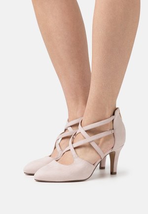 Jasnoróżowe zamszowe szpilki z ostrym noskiem, z przecinającymi się paskami na stopie i zwężającym się obcasem. Gładka faktura i minimalne detale.