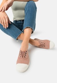 Jasnoróżowe sneakersy wsuwane z płótna, biała gumowa osłona na palce i metalowe oczka na sznurówki. Z wyróżniającym się teksturowanym wzorem w kształcie litery V.