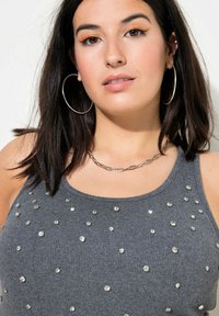 Top in maglia grigia senza maniche decorato con strass sparsi, scollo rotondo e texture a costine. Collana in catena metallica e grandi orecchini a cerchio.