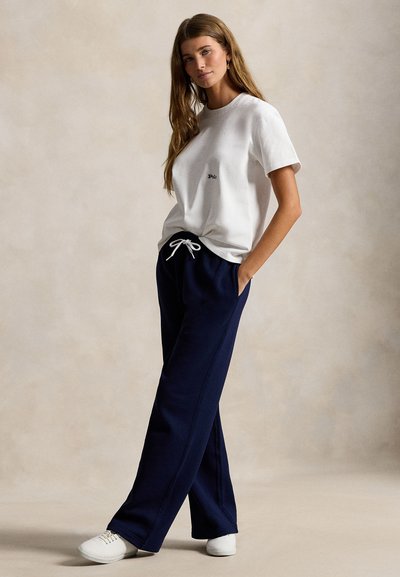 Λευκό βαμβακερό μπλουζάκι με μικρό κεντημένο λογότυπο, συνδυασμένο με άνετη μπλε φόρμα σκούρου μπλε χρώματος με κορδόνι στη μέση και πλαϊνές τσέπες. Λευκά παπούτσια.