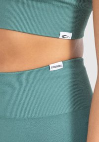 Un crop top côtelé teal et un legging taille haute assorti, arborant des étiquettes de marque contrastantes brodées à la taille et à l'ourlet.