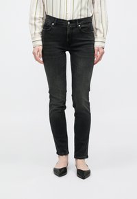 Fekete, szűk fazonú farmer enyhe mos�ással, öt zsebbel és ezüst színű kiegészítőkkel. Fekete, hegyes orrú balerinacipővel és csíkos inggel párosítva.