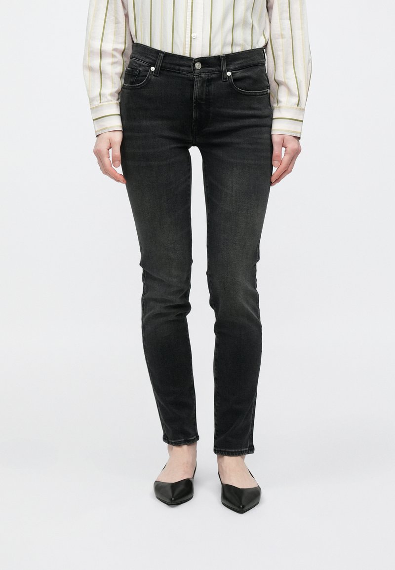 Fekete, szűk fazonú farmer enyhe mosással, öt zsebbel és ezüst színű kiegészítőkkel. Fekete, hegyes orrú balerinacipővel és csíkos inggel párosítva.