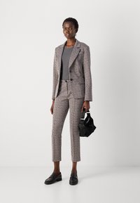 Checked blazer and trousers set in a light and dark color pattern, with a fitted design, complemented by a gray top and a black handbag.