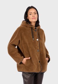 Braune Fleecejacke mit Kapuze, ausgestattet mit einer knöpfbaren Vorderseite, Seitentaschen und schwarzen Kordeln, die einen weichen, strukturierten Stoff zeigt.