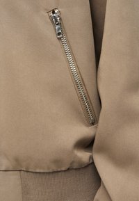 Bruine zip-up jas sectie met een gladde stoffen textuur, zilverkleurige rits hardware en elastische tailleband details.