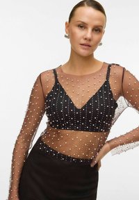 Black, fitted top with sheer, embellished long sleeves. Features pearl-like beads arranged in rows on a transparent fabric. V-neck design.