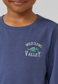 Blauwe langärmsgemerkte katoen shirt met een ronde hals en een geborduurd ontwerp van een dinosauruss en de tekst "WILD CLAWS VALLEY."