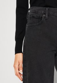 Jean en denim noir avec un design classique à cinq poches, dotés d'une fermeture éclair, de coutures discrètes et d'une texture lisse.
