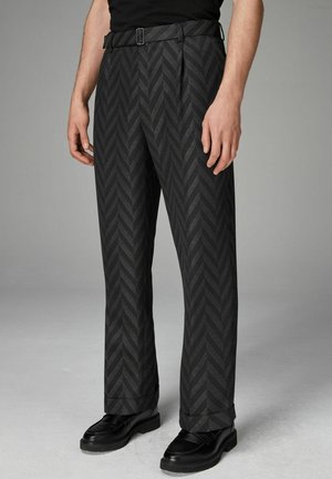 Schwarze Hosen mit einem Fischgrätmuster, geradem Schnitt und einem Gürtel mit einer Metallschnalle. Tragen mit schwarzen Schuhen, die die Textur und das Design hervorheben.