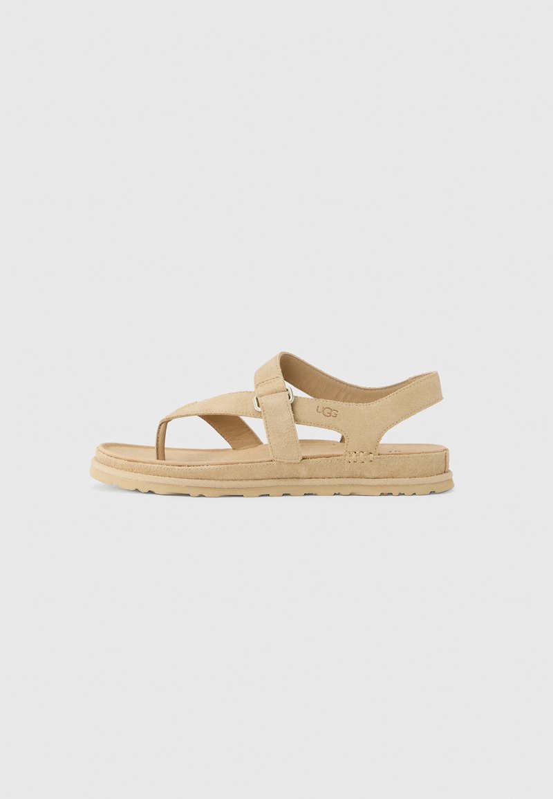 Sandale en daim beige avec bout ouvert, brides ajustables et semelle plate en caoutchouc. Présente un design minimaliste et un marquage discret sur le côté.