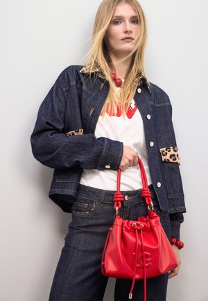 Chaqueta vaquera con detalles de estampado de leopardo, camiseta gráfica blanca, vaqueros oscuros y un pequeño bolso rojo de cuero con cordón y detalle del logo.
