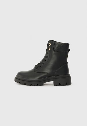 Botines de cuero negro hasta el tobillo con parte trasera texturizada, ojetes dorados, punta redondeada y suela de goma gruesa con surcos profundos para mayor tracción.