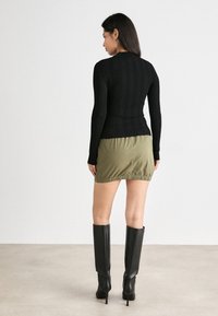Melnas ribotas garām piedurknēm tops, kas kombinēts ar zaļu svārku ar elastīgu jostu. Modelis valkā melnus augstpapēžu zābakus līdz ceļgaliem.