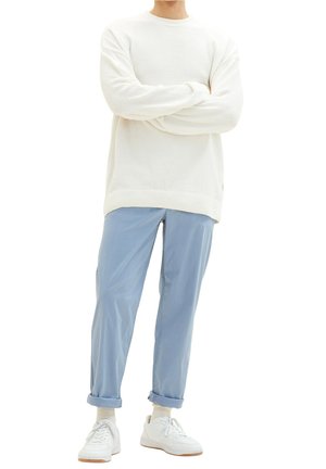 Un pull blanc texturé associé à un pantalon bleu clair à revers et des baskets blanches avec des accents marron. Design simple, coupe décontractée.